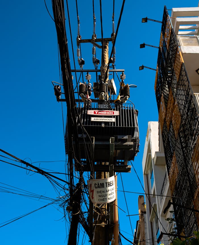 services-03 High-voltage transformer and wires against a clear blue sky in an urban setting.