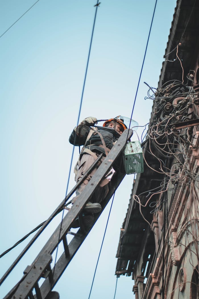 services-04 Electrician working on a building's power lines from a ladder, showcasing urban electrical maintenance.