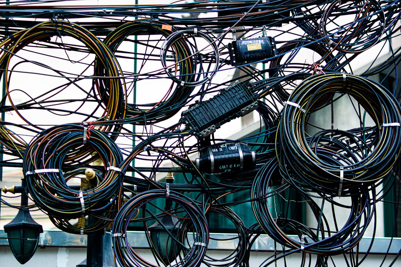 services-01 Intricate network of tangled power and communication cables outdoors.
