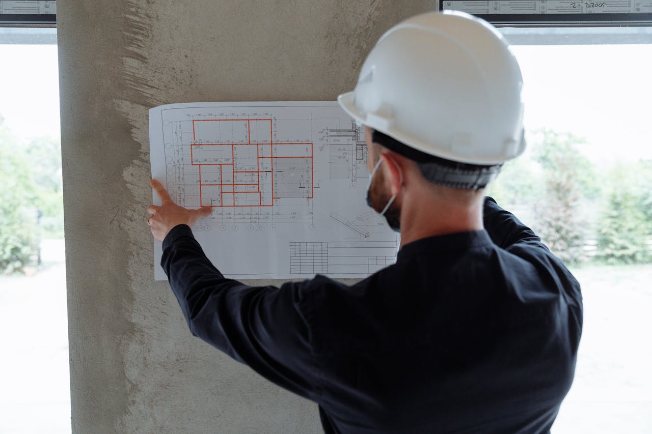services-02 Engineer in hardhat reviewing architectural floor plans at construction site.